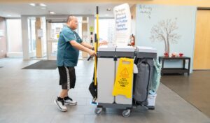 A worker pushing a cleaning cart through a hallway