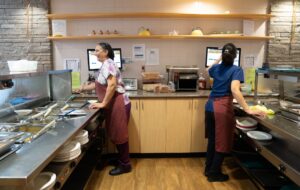 Two workers serving in a kitchen and keeping the food dispensing area clean