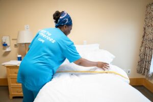 A worker carefully fitting bedding to a bed